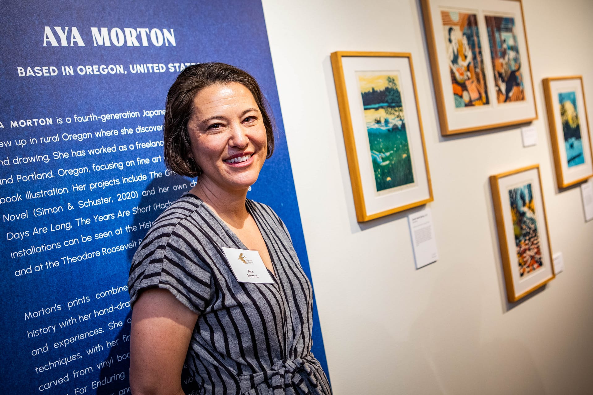 a woman smiles next to framed woodblock prints on a wall