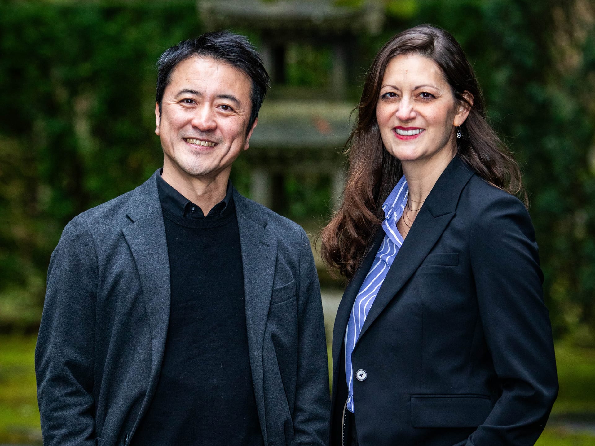 two people standing and smiling in front of a tall stone lantern