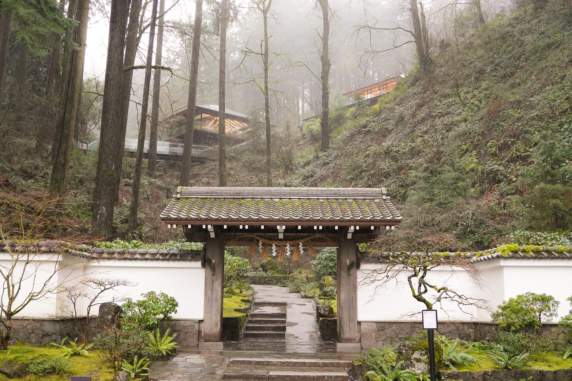 Japanese wooden gate flanked by stucco walls in front of a chilly and bare winter hillside