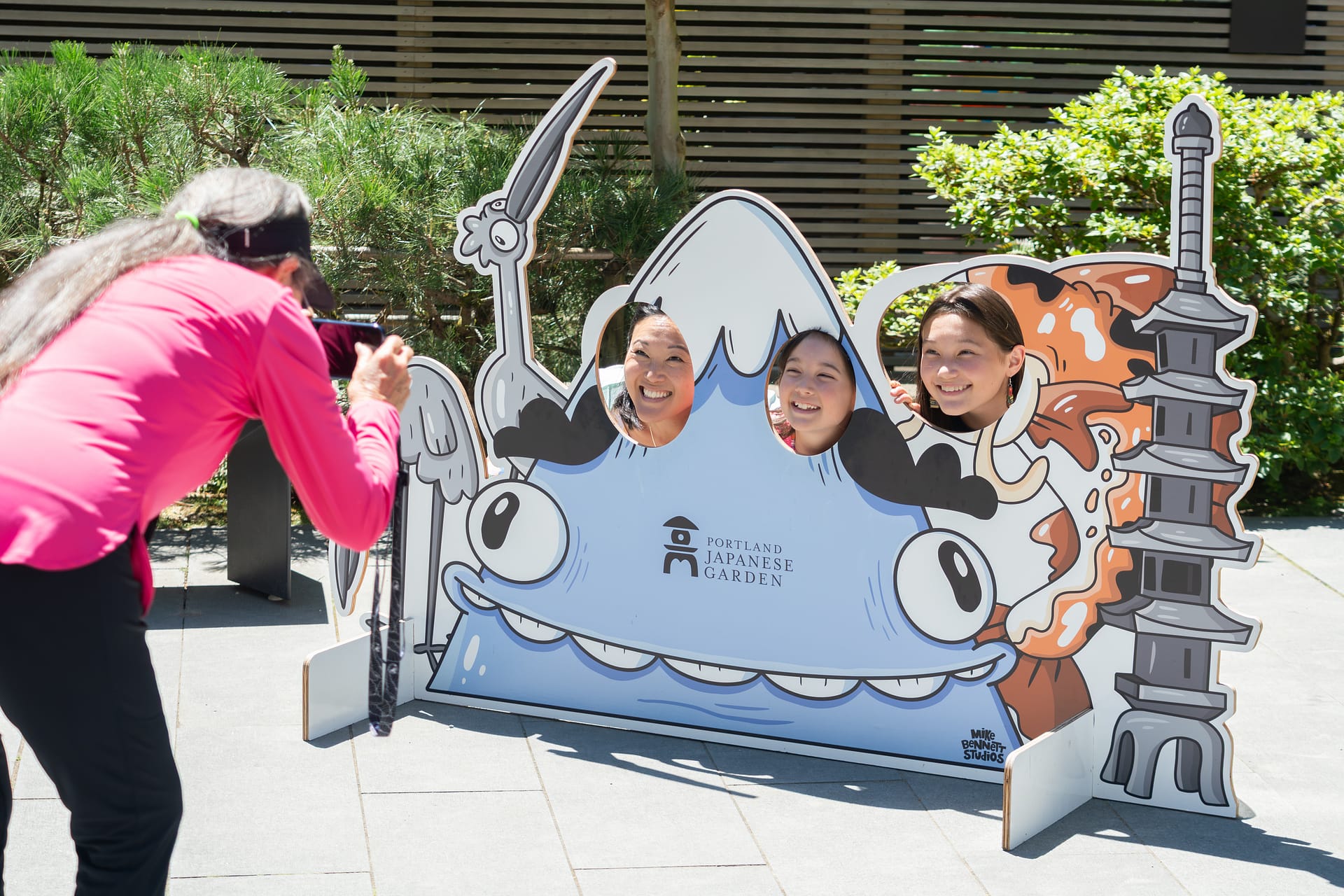 a family sticks their faces in through holes in a large photo standee featuring a cartoon Mt. Hood