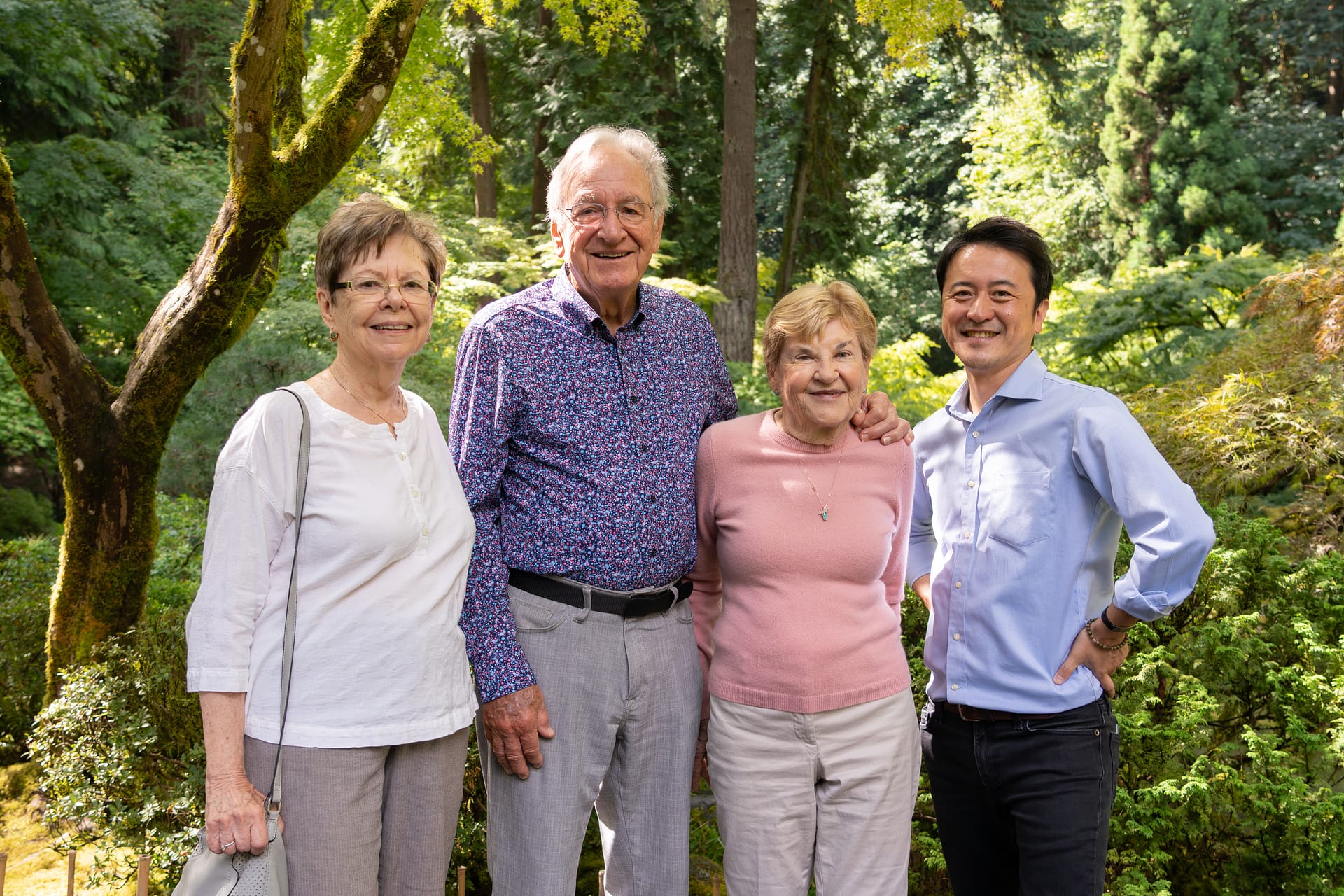 four people smiling for a camera, with trees behind them