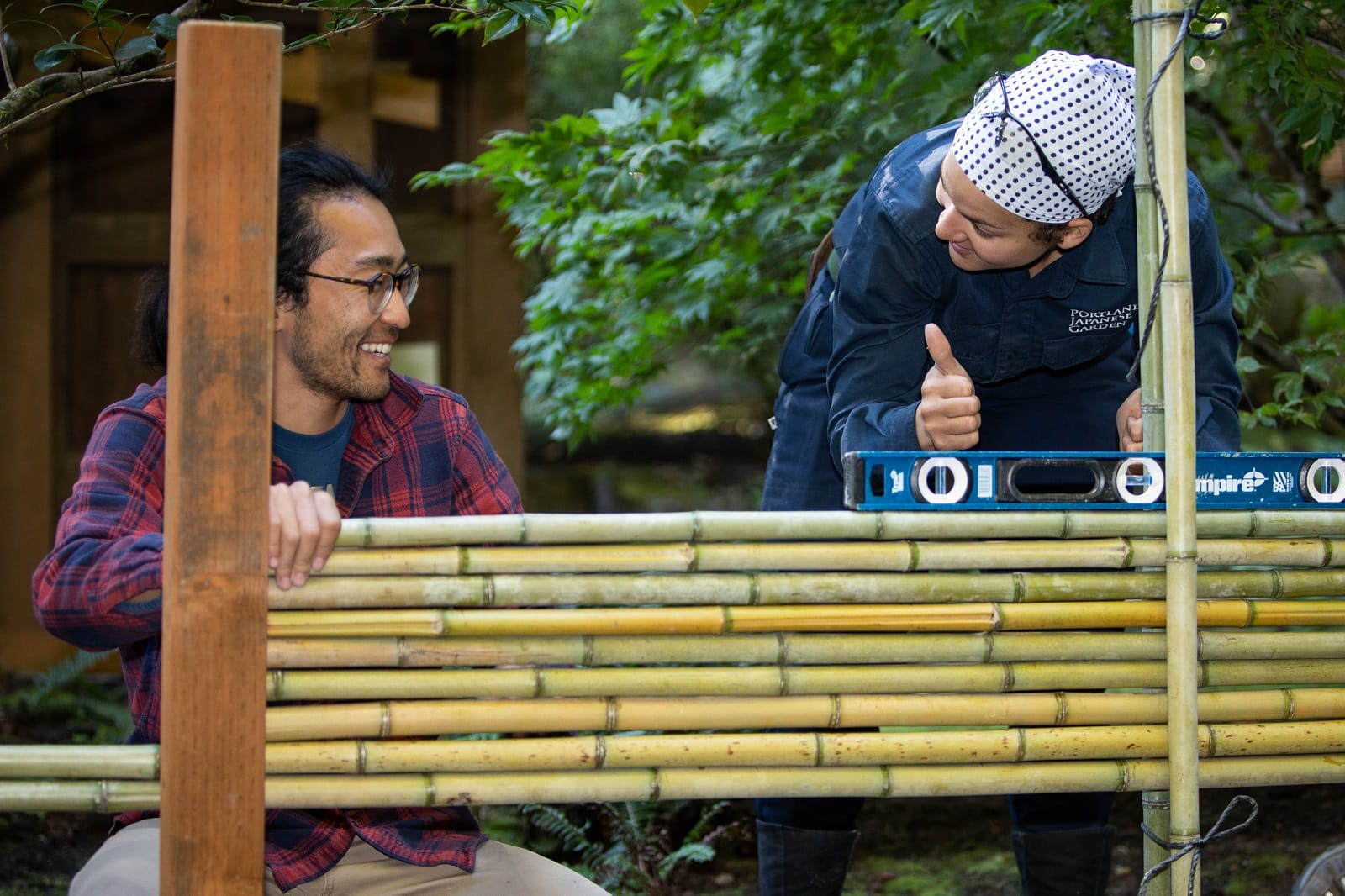 Gardener gives thumbs up to student as they contruct a fence together