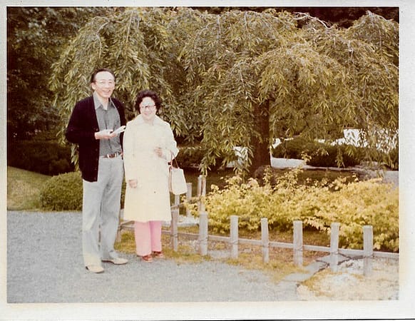 A husband and wife in the either 1970s or 80s standing next to a weeping cherry tree