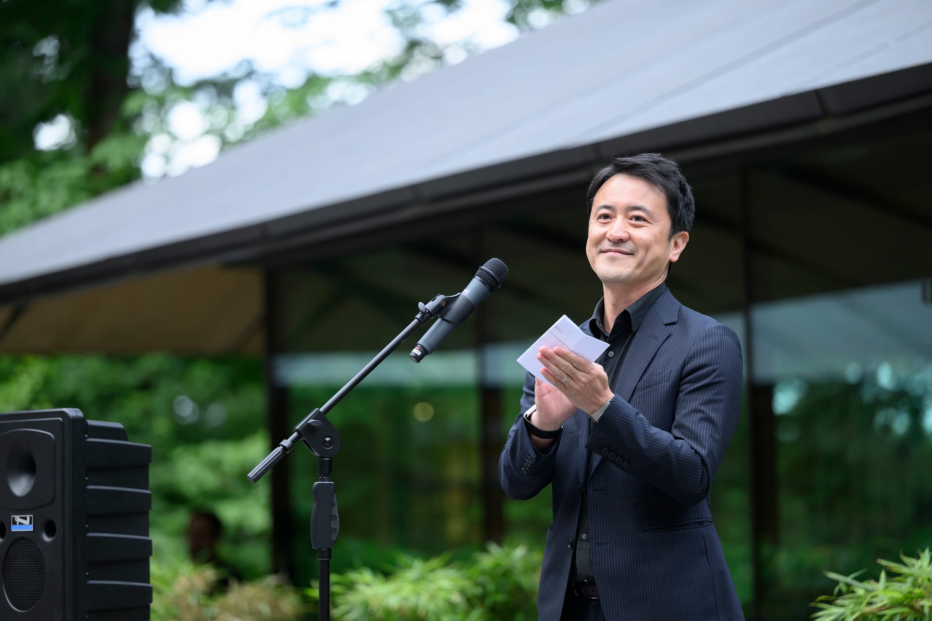 Aki Nakanishi standing at a microphone in Portland Japanese Garden.