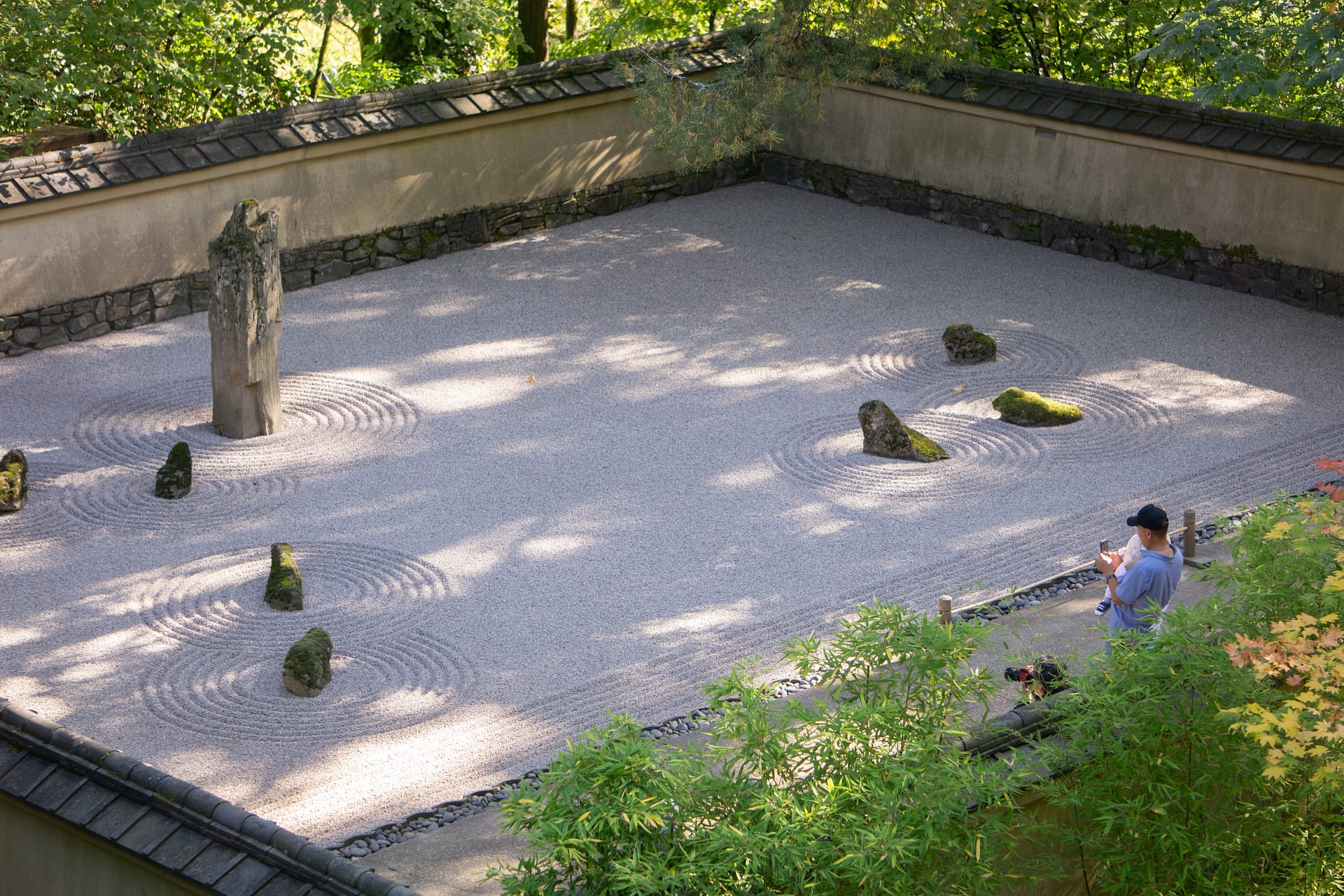 A father holds his child taking a photo of a raked gravel garden