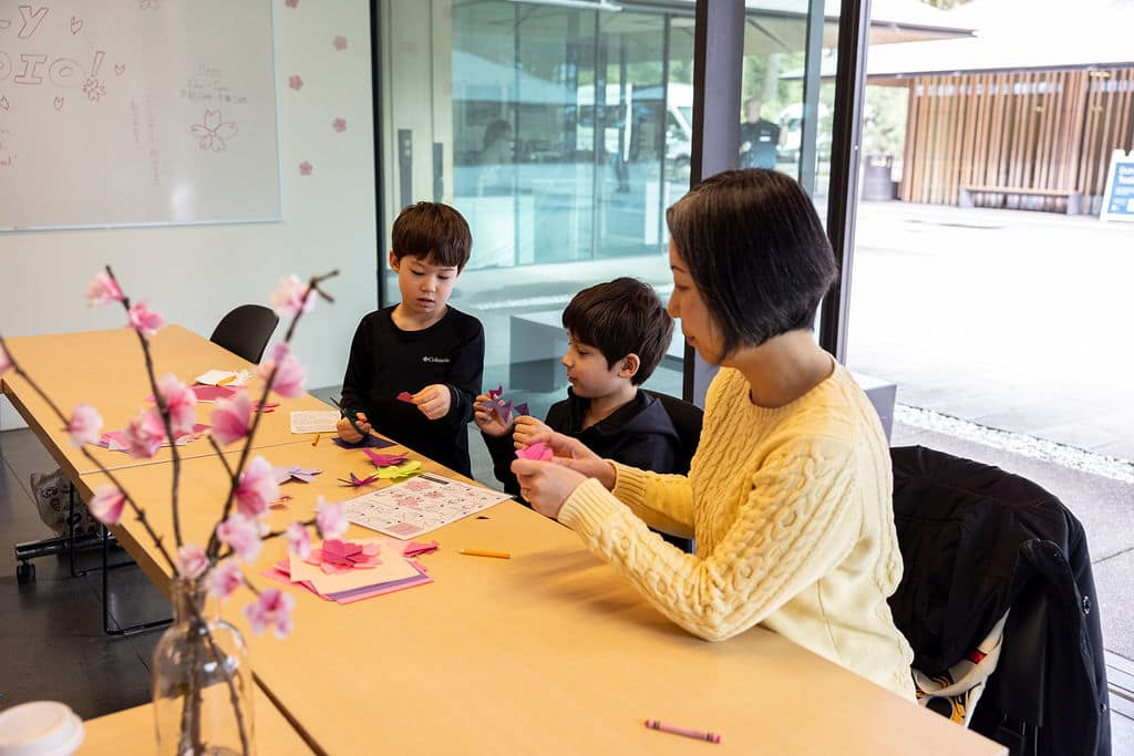 Woman and two children doing origami inside a glass building.