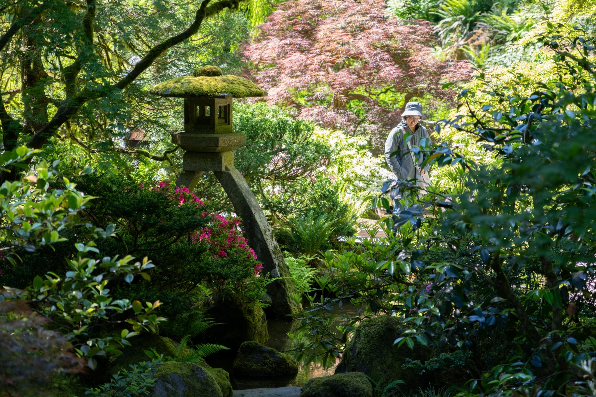 a large stone lantern in shadow next to a person walking in bright sunlight