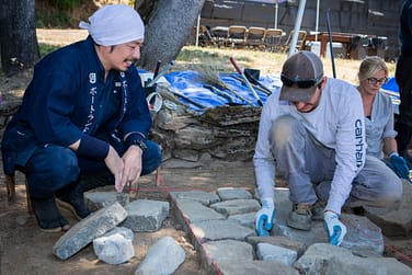A person practicing placing stones down for a pathway while a teacher supervises.