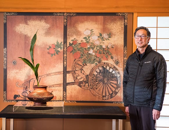a man smiling next to a display of ikebana
