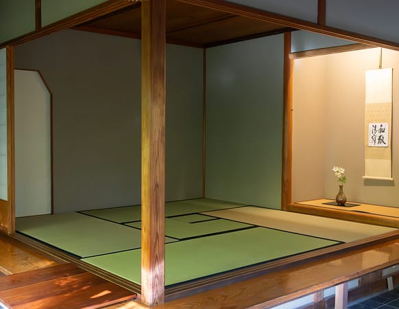 a tea room with tatami mats and an alcove with a flower in a vase in it and a scroll on the wall