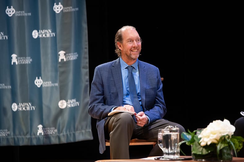 Thomas Hill sitting in a chair on stage at Japan Institute's New York Peace Symposium.