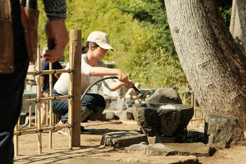 A woman crouched down with a hose filling a basin with water.