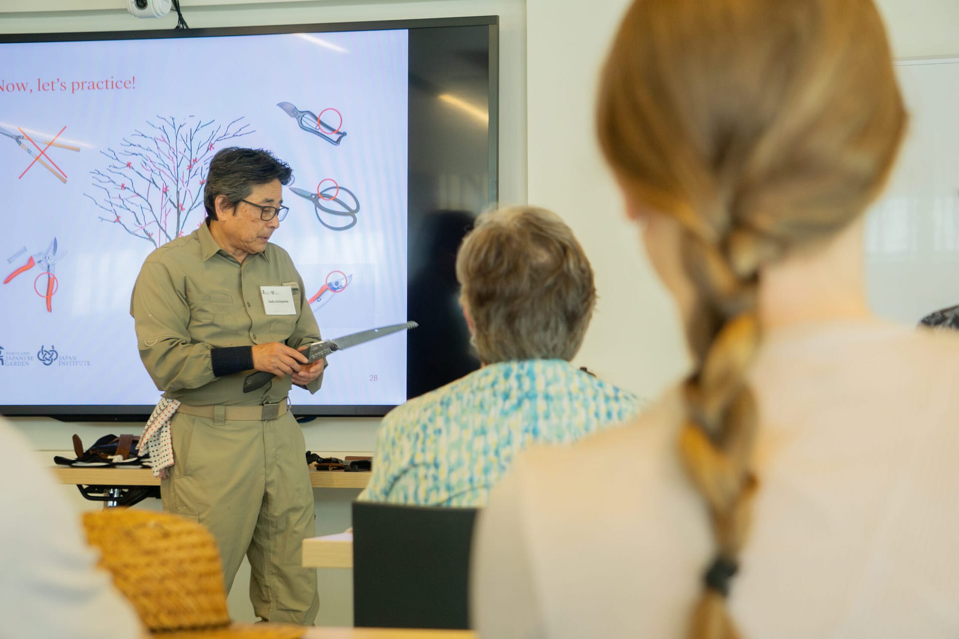 A teacher holds a saw in front of a classroom.