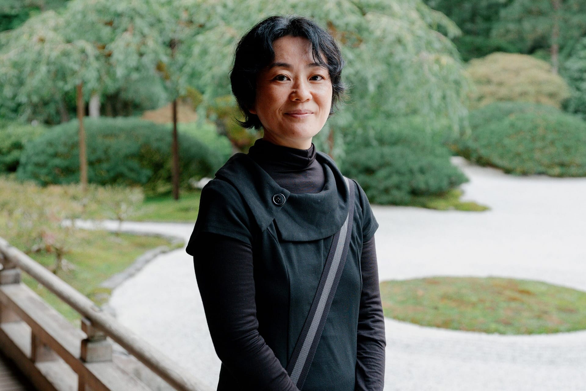 A woman wear a black sweater standing in front of a Japanese garden.