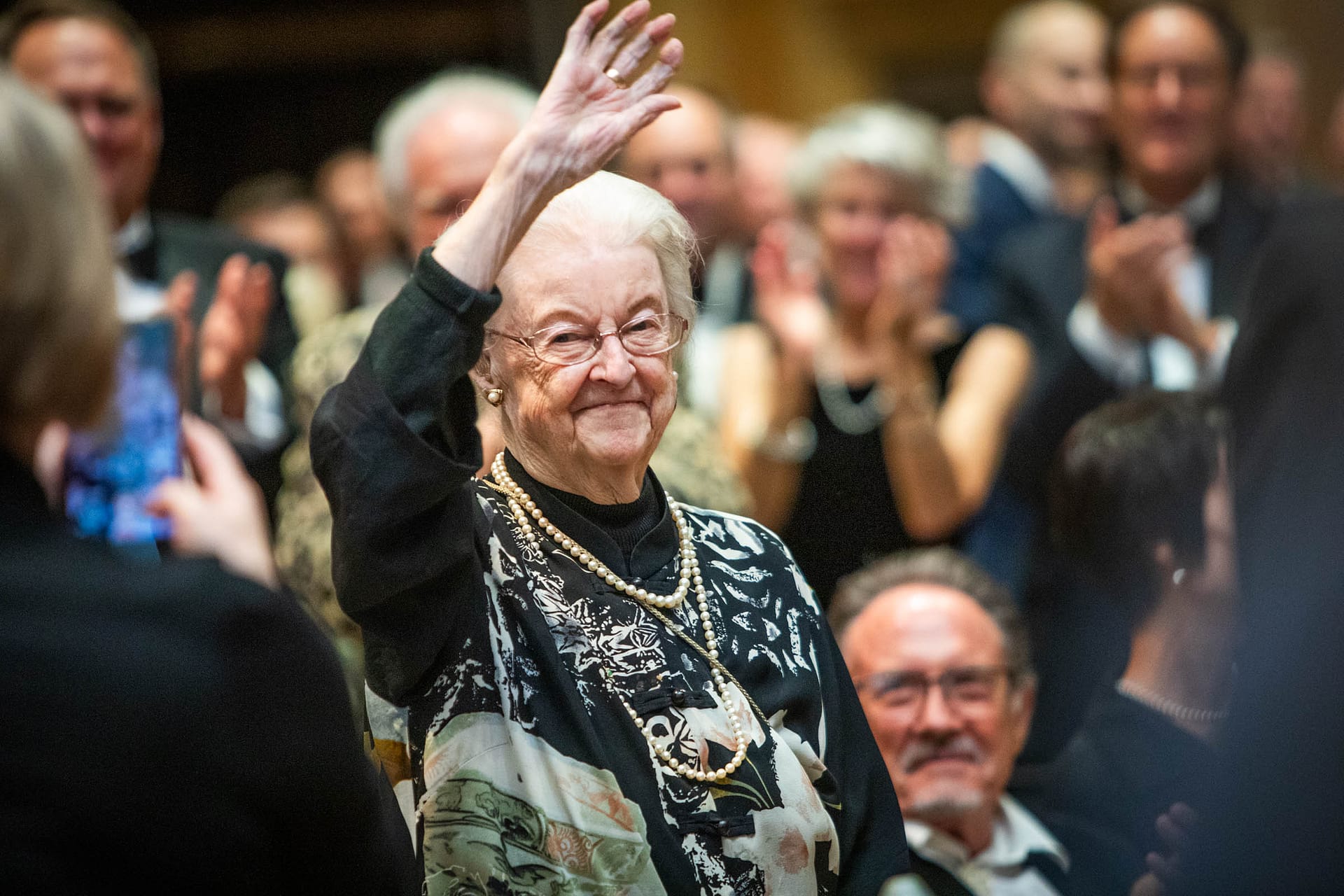 Maggie Drake standing, waving to people at a gala.