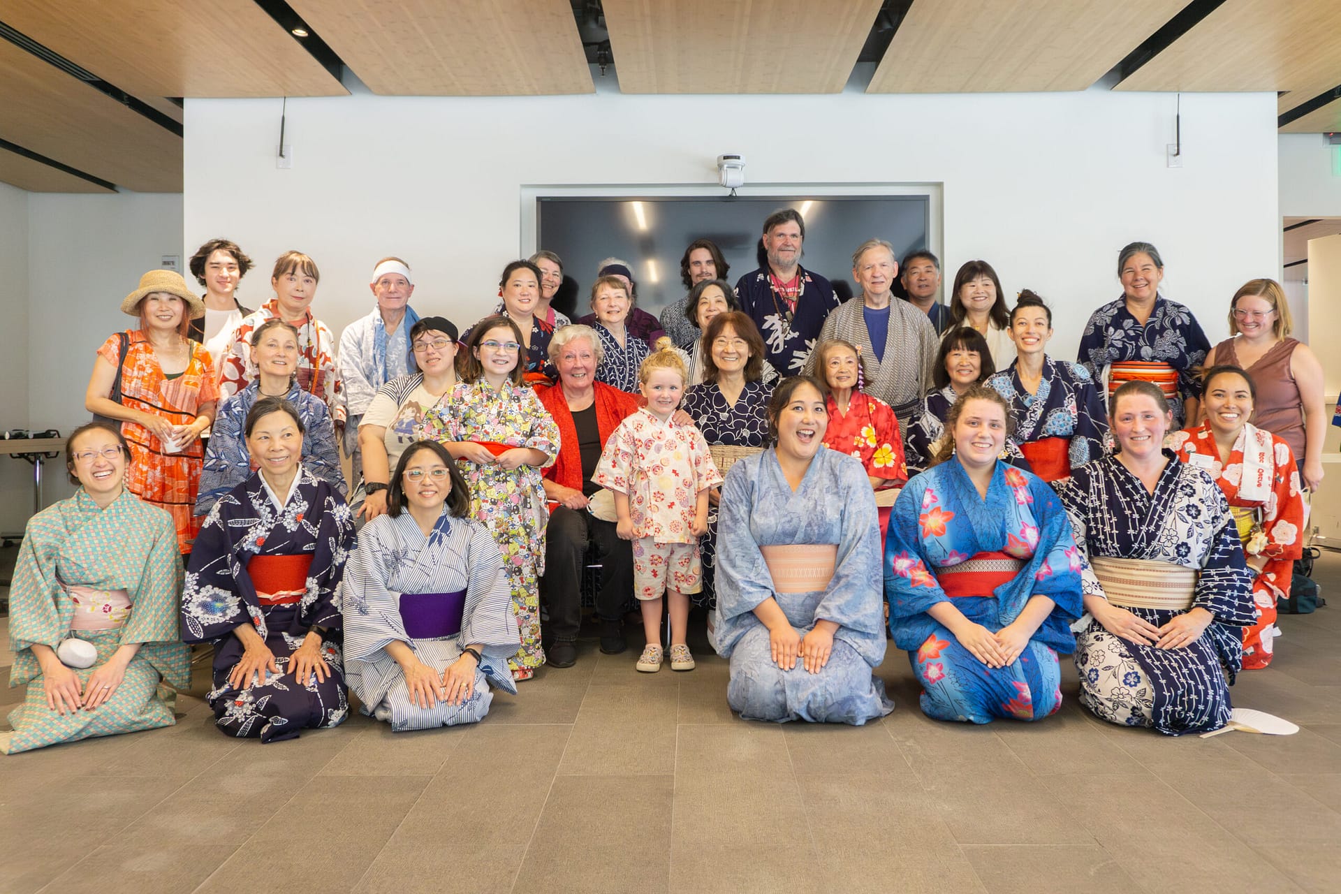 A large group dressed in yukata pose for a photo inside.