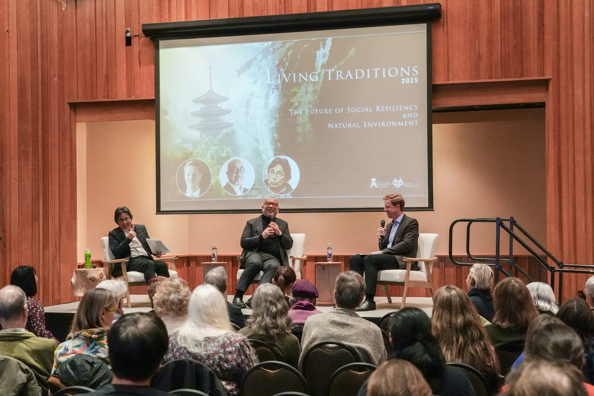 Three people sitting in chairs on stage in front of an audience.