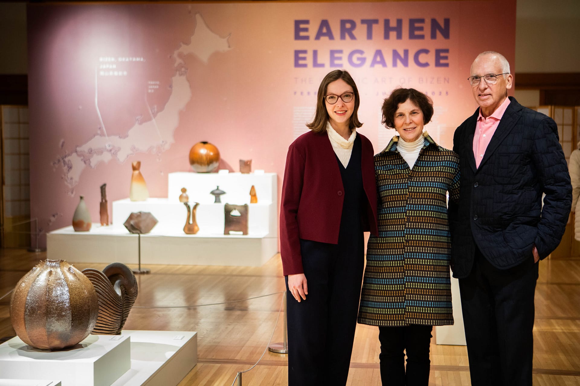 The owners of an art collection stand by the art next to their daughter in an art gallery.