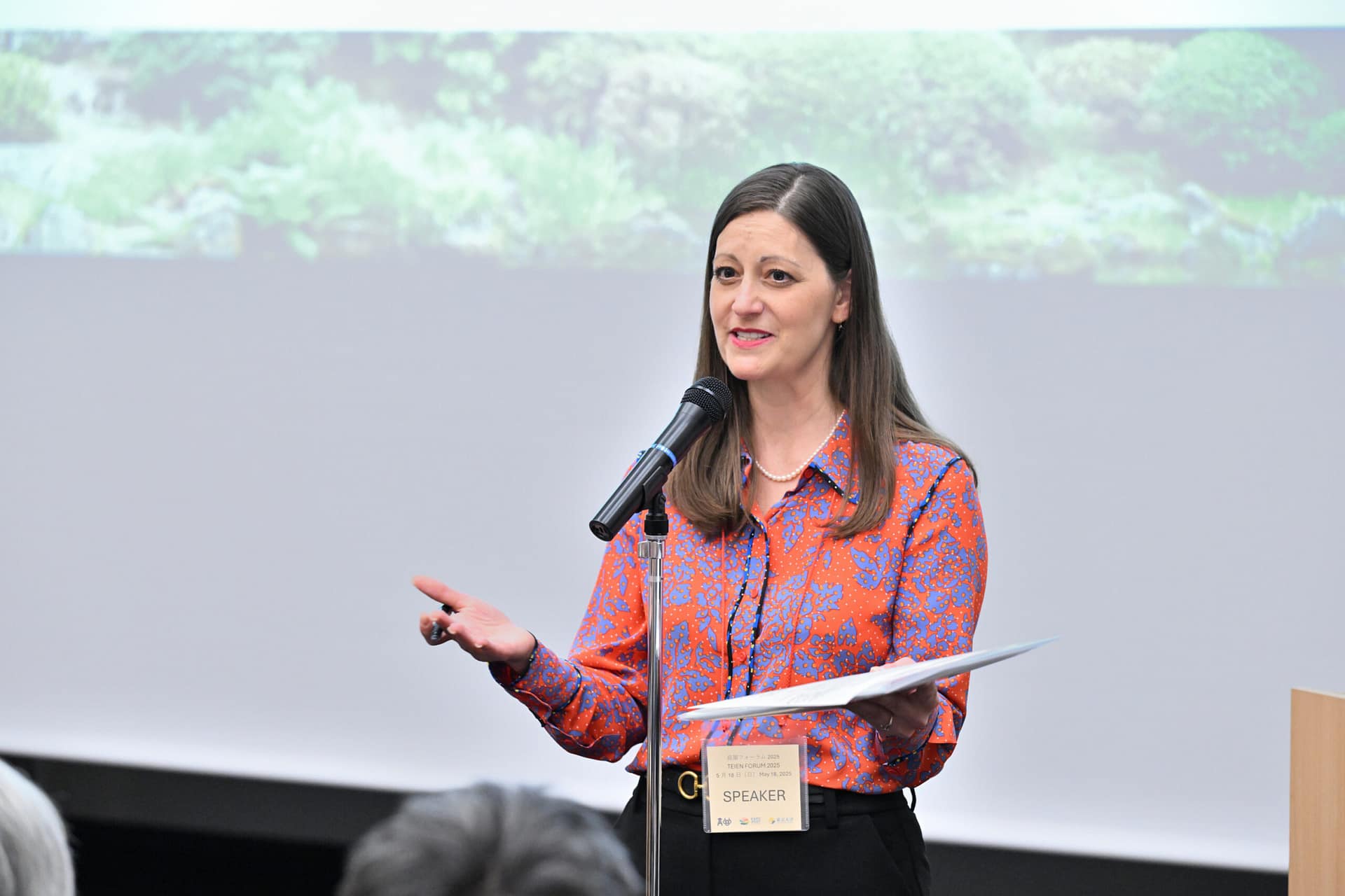 a woman stands in front of a microphone, speaking