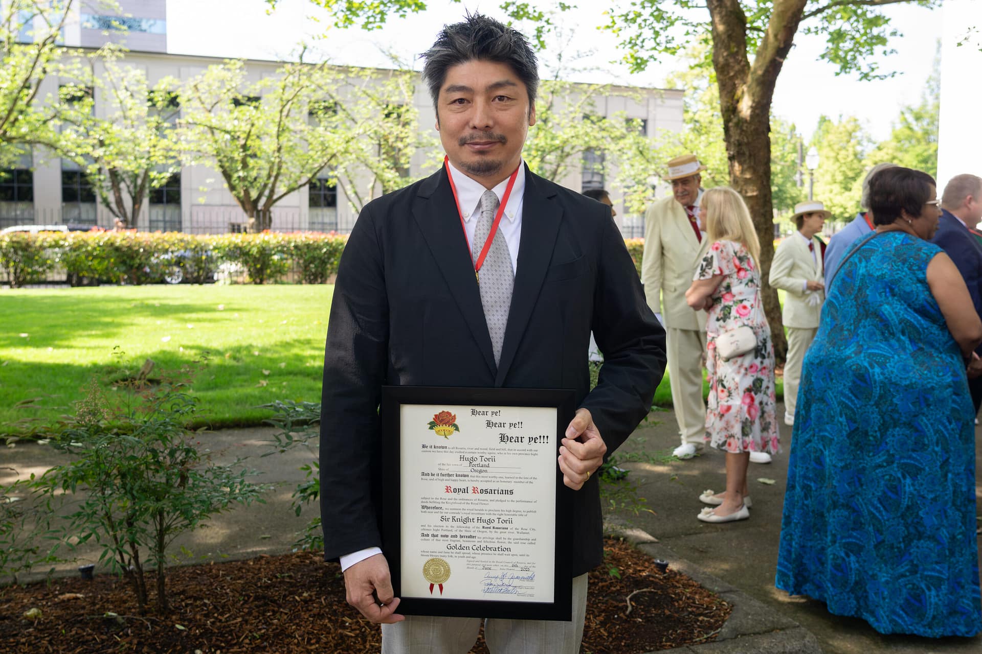 A man in a suit holds a framed certificate.