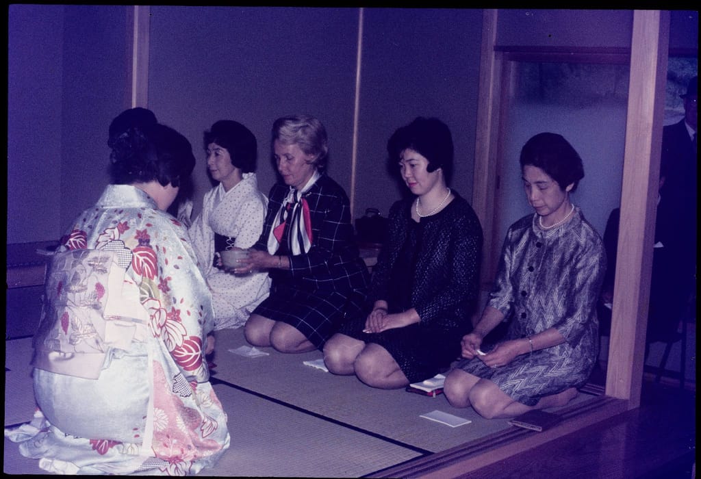 four tea ceremony guests kneeling on tatami mats while a tea ceremony host prepares